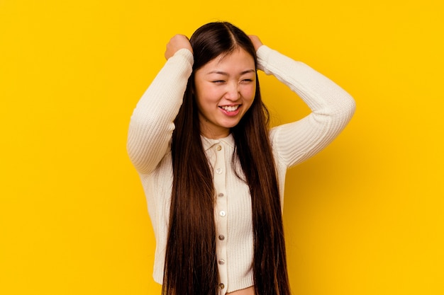 Jovem mulher chinesa isolada na parede amarela, cobrindo as orelhas com as mãos.