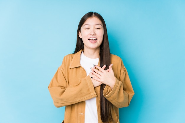Jovem mulher chinesa posando em azul isolada rindo mantendo as mãos no coração, o conceito de felicidade.