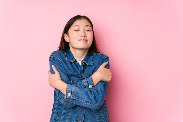 Jovem mulher chinesa posando em um fundo rosa isolado abraços, sorrindo despreocupada e feliz.