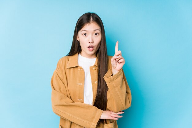 Jovem mulher chinesa posando em uma parede azul isolada tendo uma ótima ideia, o conceito de criatividade.