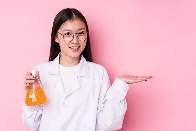 Jovem mulher científica chinesa isolada, mostrando um espaço de cópia na palma da mão e segurando a outra mão na cintura.