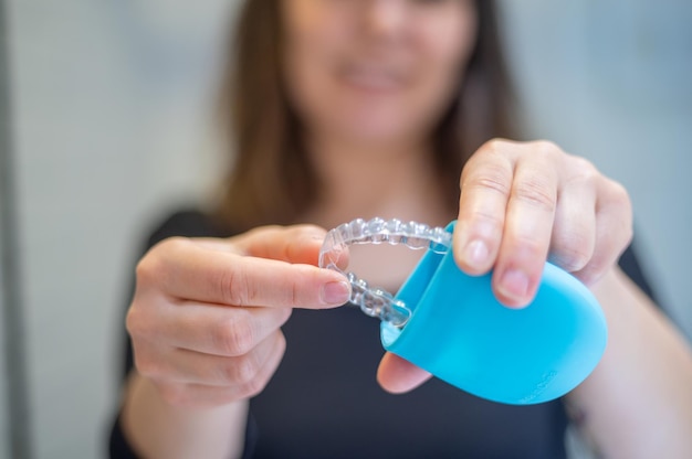 Jovem mulher colocando com dois dedos um alinhador dental invisível dentro de uma caixa enquanto sorri.