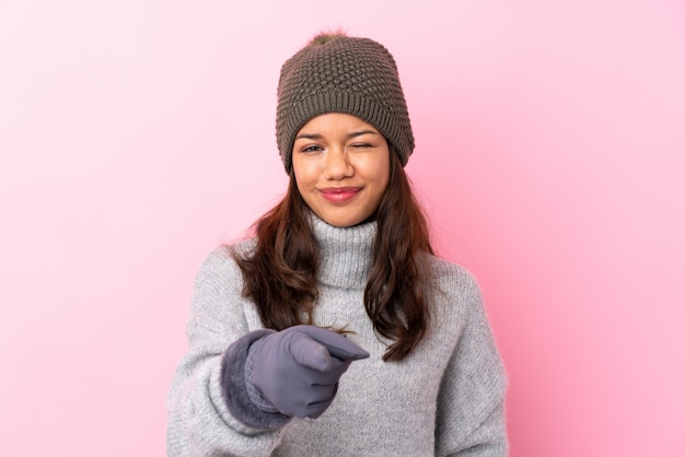 Jovem mulher colombiana com chapéu de inverno sobre parede rosa isolada aponta o dedo para você