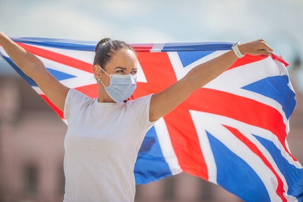 Jovem mulher com bandeira britânica usa uma máscara ao ar livre.