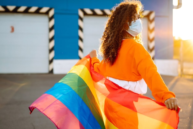 Jovem mulher com bandeira LGBT e máscara protetora