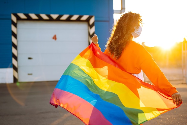Jovem mulher com bandeira LGBT e máscara protetora