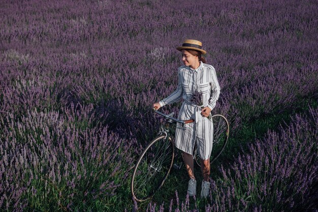 Jovem mulher com bicicleta retrô e buquê de lavanda no fundo do campo de flores violetas