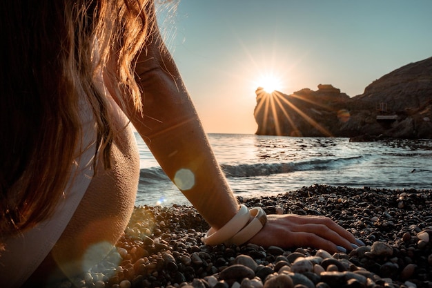 Jovem mulher com cabelo comprido em maiô branco e pulseiras estilo boho praticando ao ar livre no tapete de ioga à beira-mar em um pôr do sol Rotina de fitness ioga feminina Harmonia e meditação de estilo de vida saudável