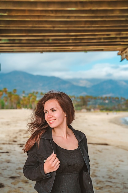 jovem mulher com cabelo comprido fica perto do cais na praia em santa barbara, califórnia, eua