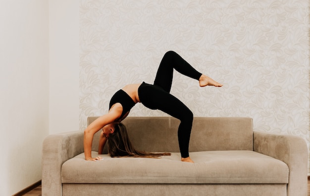 Jovem mulher com cabelo comprido, instrutor de fitness em roupa esportiva preta, fazendo alongamento e pilates