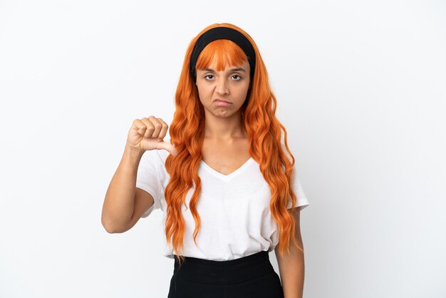 Jovem mulher com cabelo laranja isolado no fundo branco, mostrando o polegar para baixo com expressão negativa