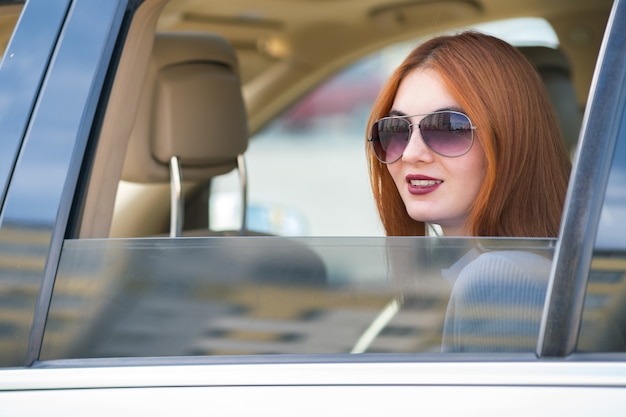 Jovem mulher com cabelo vermelho e óculos de sol, viajando de carro