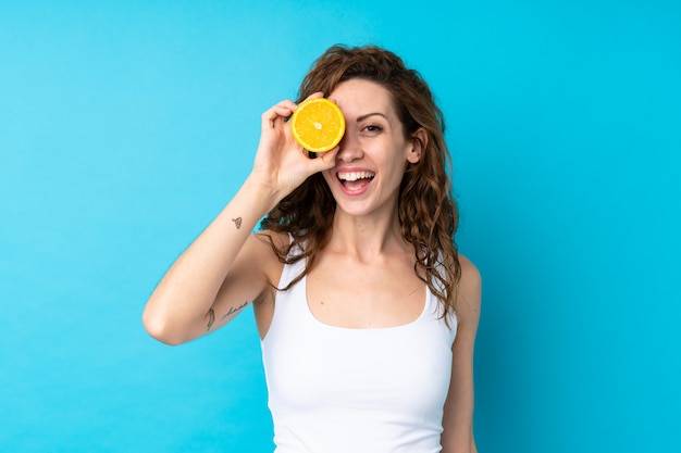 Jovem mulher com cabelos cacheados, segurando uma laranja sobre azul isolado