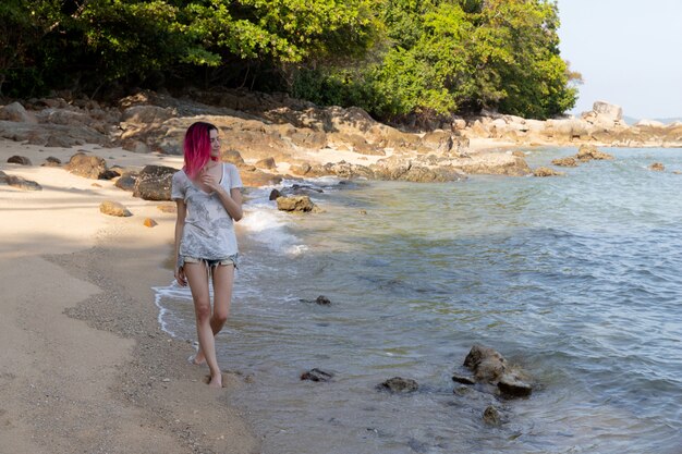 Jovem mulher com cabelos rosa vibrantes, andando perto do mar ou oceano.