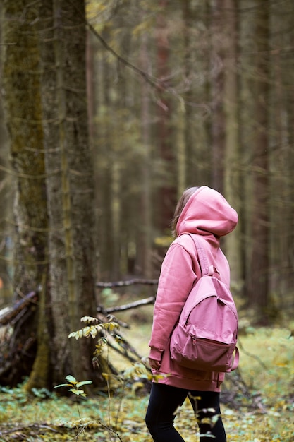 Jovem mulher com capuz rosa caminhando na floresta de outono e curtindo a natureza. Formato vertical. Foto de alta qualidade. Outono. Vista traseira. Copie o espaço