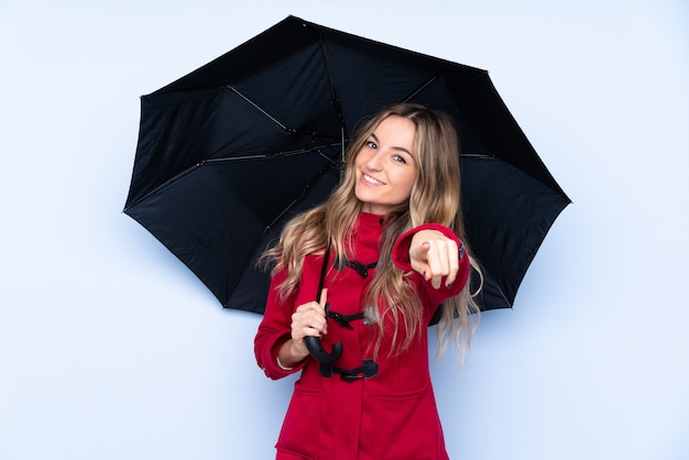Jovem mulher com casaco de inverno e segurando um guarda-chuva aponta o dedo para você com uma expressão confiante