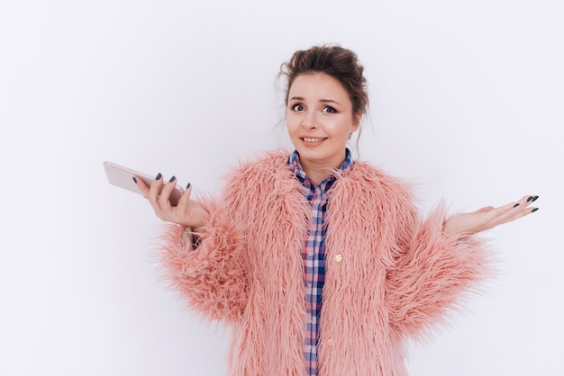 Foto jovem mulher com casaco de pele rosa, segurando o telefone. parede cinza isolada