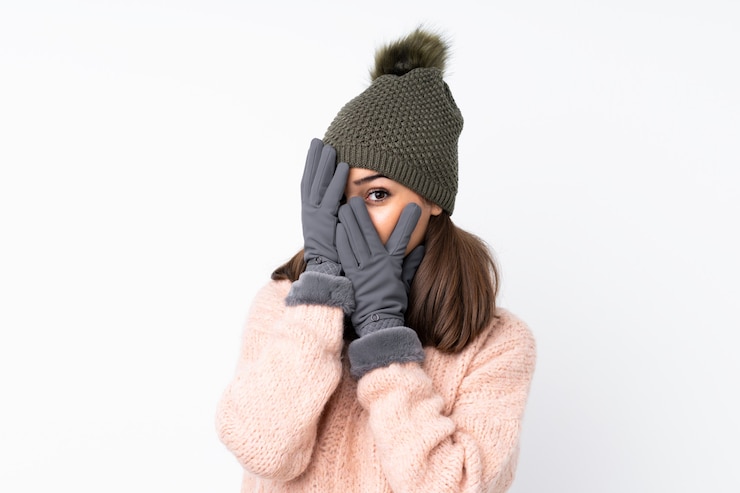 Foto jovem mulher com chapéu de inverno, cobrindo os olhos e olhando por entre os dedos