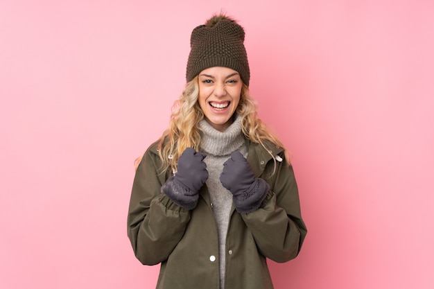 Jovem mulher com chapéu de inverno isolado na parede rosa comemorando uma vitória