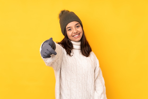 Jovem mulher com chapéu de inverno na parede amarela isolada com o polegar para cima