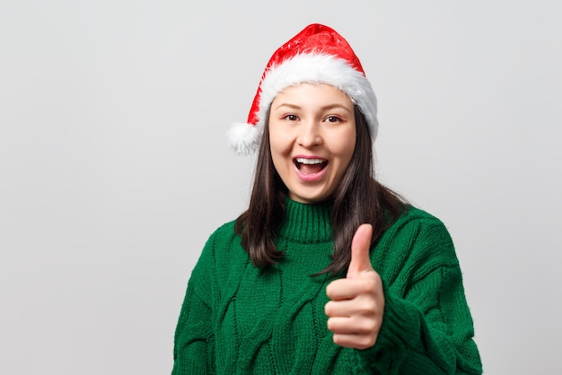 Jovem mulher com chapéu de Natal, mostrando o polegar para cima gesto. Sobre um fundo branco.