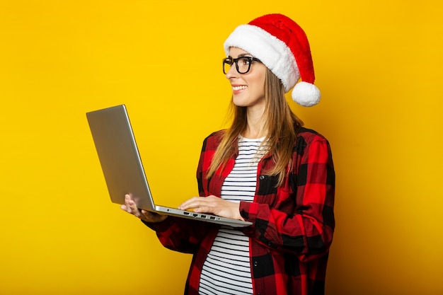 Jovem mulher com chapéu de Papai Noel e camisa vermelha em uma gaiola segurando um lapto