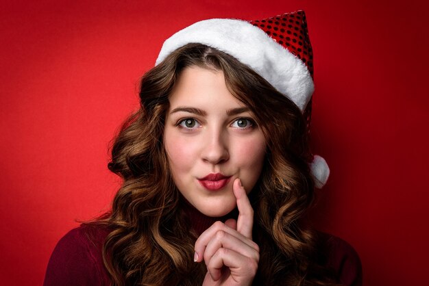 Jovem mulher com chapéu de Papai Noel em fundo vermelho. Conceito de Natal e ano novo.
