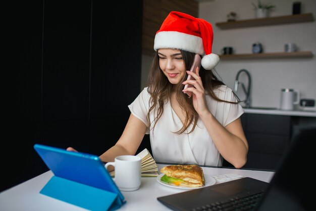 Jovem mulher com chapéu de Papai Noel na cozinha