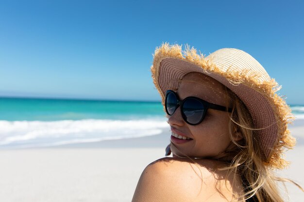 Jovem mulher com chapéu sorrindo na praia