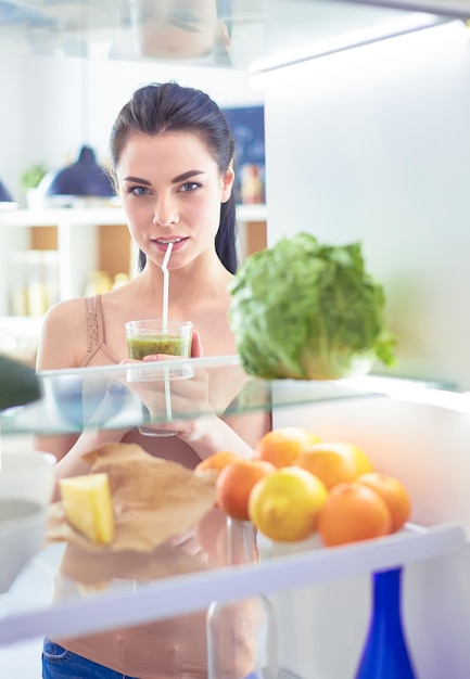 Jovem mulher com copo de saboroso smoothie saudável na mesa na cozinha