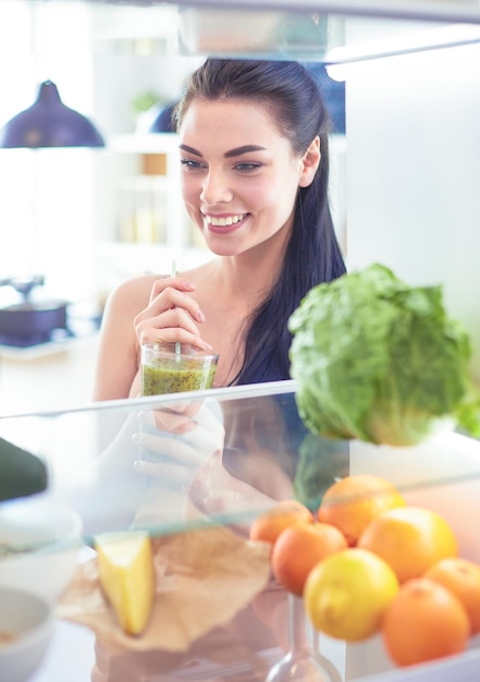 Foto jovem mulher com copo de saboroso smoothie saudável na mesa na cozinha