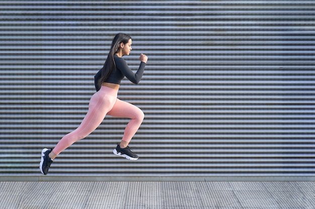Jovem mulher com corpo apto, pulando e correndo. Modelo feminino em roupas esportivas se exercitando