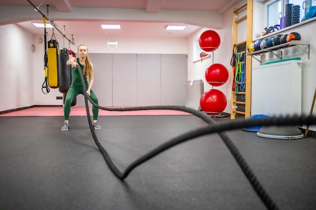 Jovem mulher com corpo perfeito fazendo exercícios crossfit com uma corda no ginásio