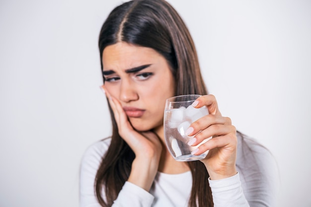 Jovem mulher com dentes sensíveis e mão segurando um copo de água fria com gelo.