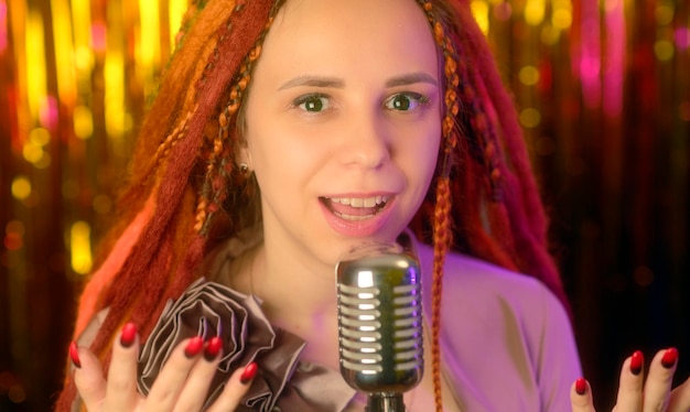 Jovem mulher com dreadlocks de gengibre falando no microfone realizando show de standup Retrato de mulher tagarelando com microfone no estúdio