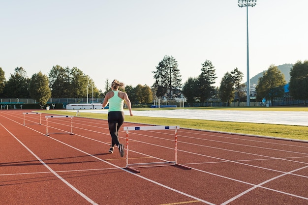Jovem mulher com excesso de peso correndo e saltando obstáculos em uma pista de atletismo em um dia ensolarado de verão