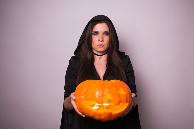 Jovem mulher com fantasia de bruxa de halloween com abóbora amarela.