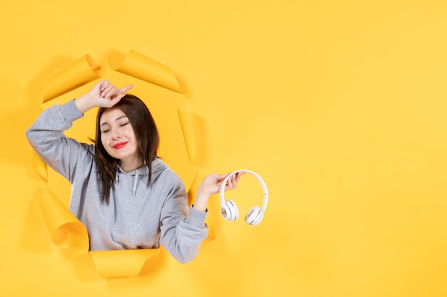 jovem mulher com fones de ouvido no som de música de ultrassom de fundo de papel amarelo rasgado