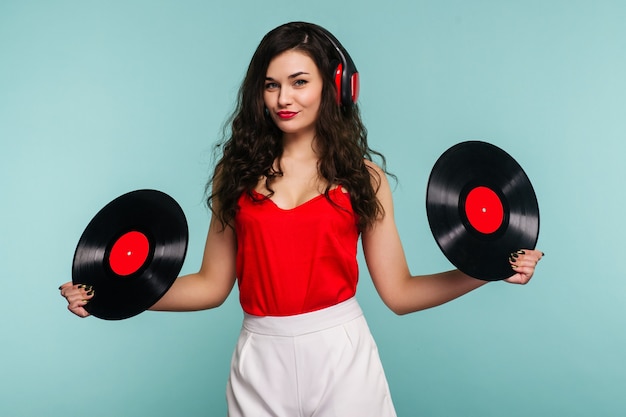 Jovem mulher com fones de ouvido, olhando para a câmera e fechando o rosto com disco de vinil em azul