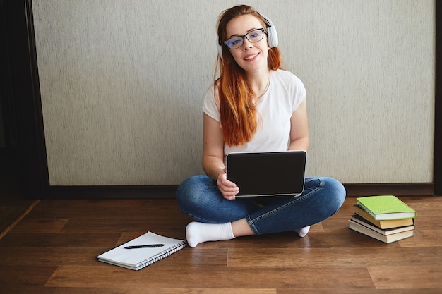 Jovem mulher com fones de ouvido trabalhar ou estudar em um laptop sentado no chão da casa. conceito de escritório em casa. trabalho a partir de casa