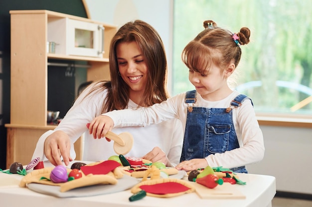 Jovem mulher com garotinha brincando com brinquedos juntos na cozinha