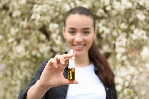 Foto jovem mulher com gotas nasais perto de árvore florescendo. conceito de alergia