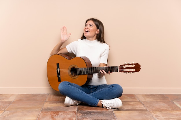 Foto jovem mulher com guitarra, sentada no chão com expressão facial de surpresa