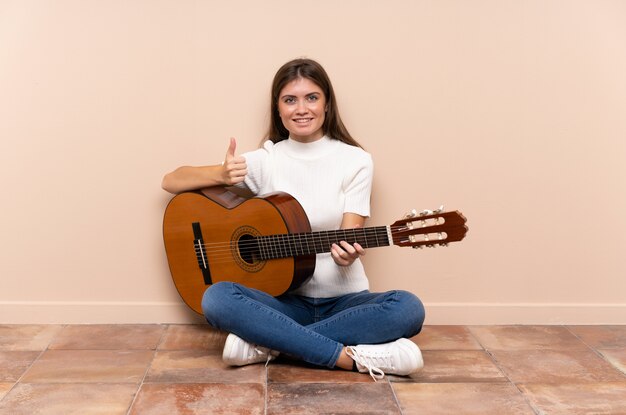 Foto jovem mulher com guitarra, sentada no chão, dando um polegar para cima gesto
