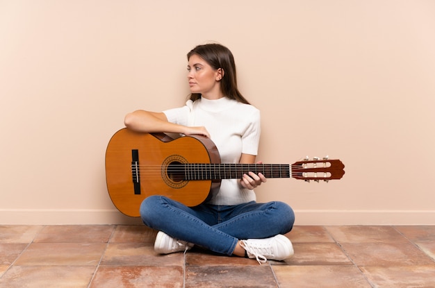 Jovem mulher com guitarra, sentada no chão, olhando de lado