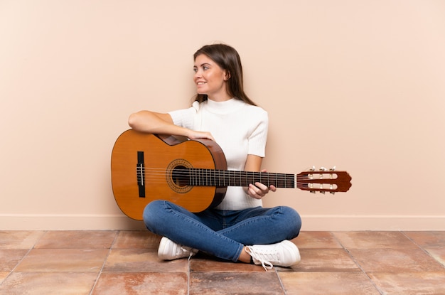 Jovem mulher com guitarra, sentada no chão, olhando para o lado