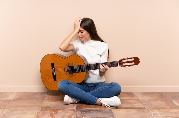 Jovem mulher com guitarra, sentada no chão, tendo dúvidas com a expressão do rosto confuso