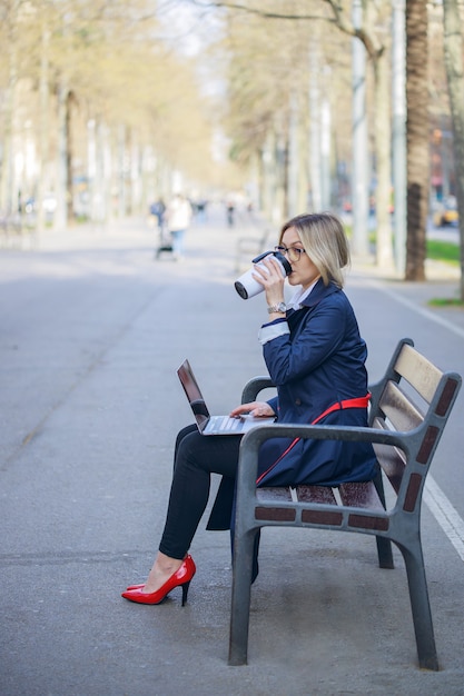 Jovem mulher com laptop em um terno de negócio bebendo uma xícara de café para viagem