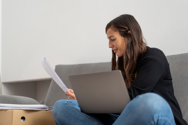 Jovem mulher com laptop telecommuting no sofá em sua casa