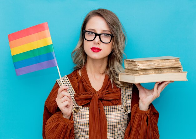 Jovem mulher com livros e bandeira LGBT no fundo azul